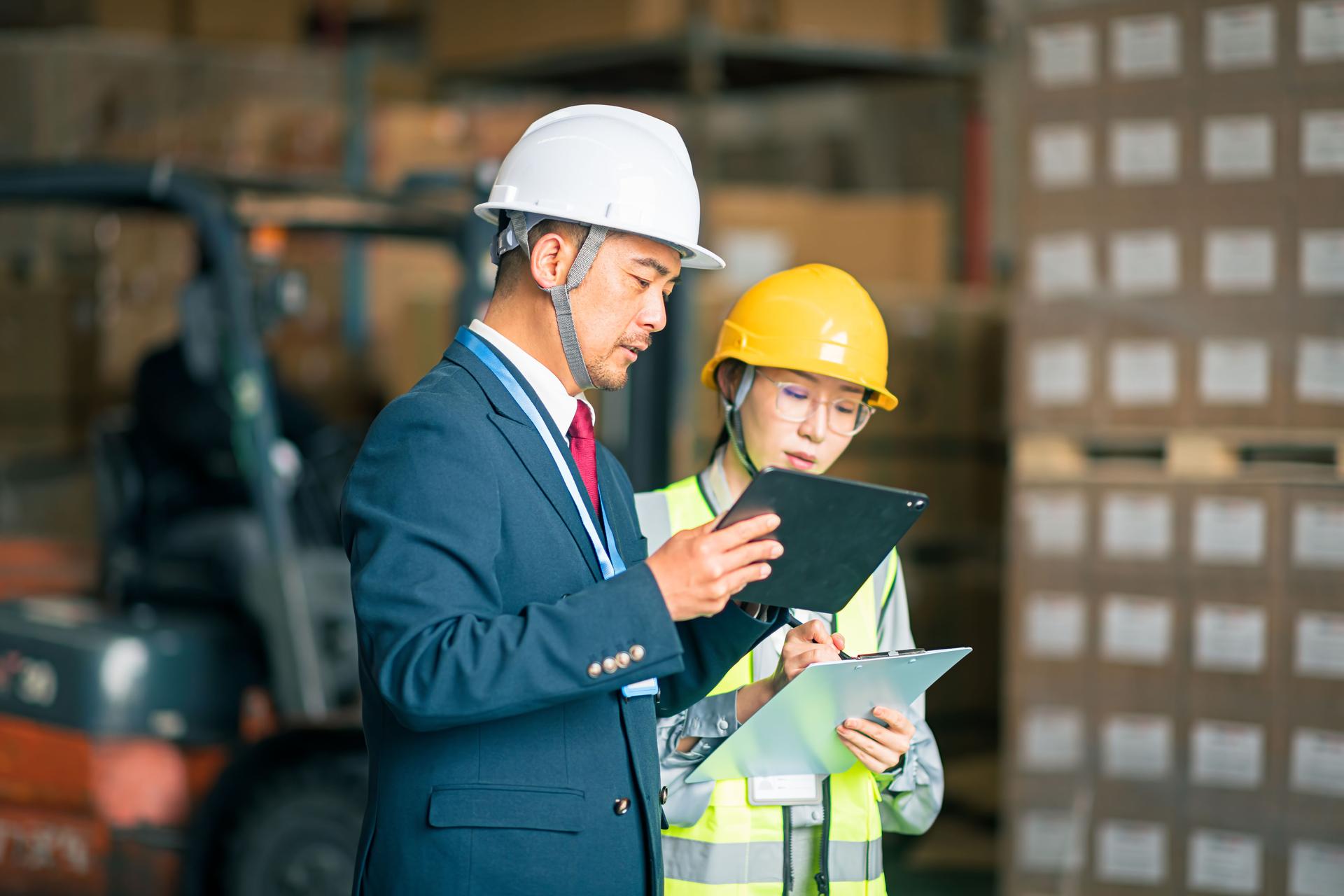 Two Asian warehouse staff are conducting logistics warehouse audits and inventory management standard operations.